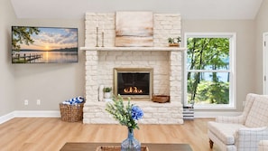 A living room with a fireplace, a large window, and a painting on the wall.