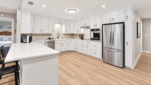 A modern kitchen with white cabinetry, stainless steel appliances, and a wooden floor.