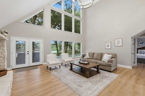A spacious living room with a high ceiling, large windows, a fireplace, and a cozy seating area.