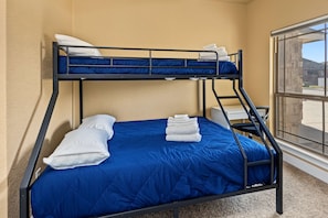 Ein Stockbett mit blauer Bettwäsche, weißen Kissen und einem Stapel weißer Handtücher.