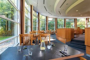 Un restaurante moderno con amplios ventanales, mesas de madera y una zona de bar central.