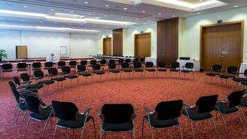 Ein Konferenzraum mit kreisförmigem Grundriss, ausgestattet mit mehreren Sitz- und Tischenreihen sowie einem Teppichboden.