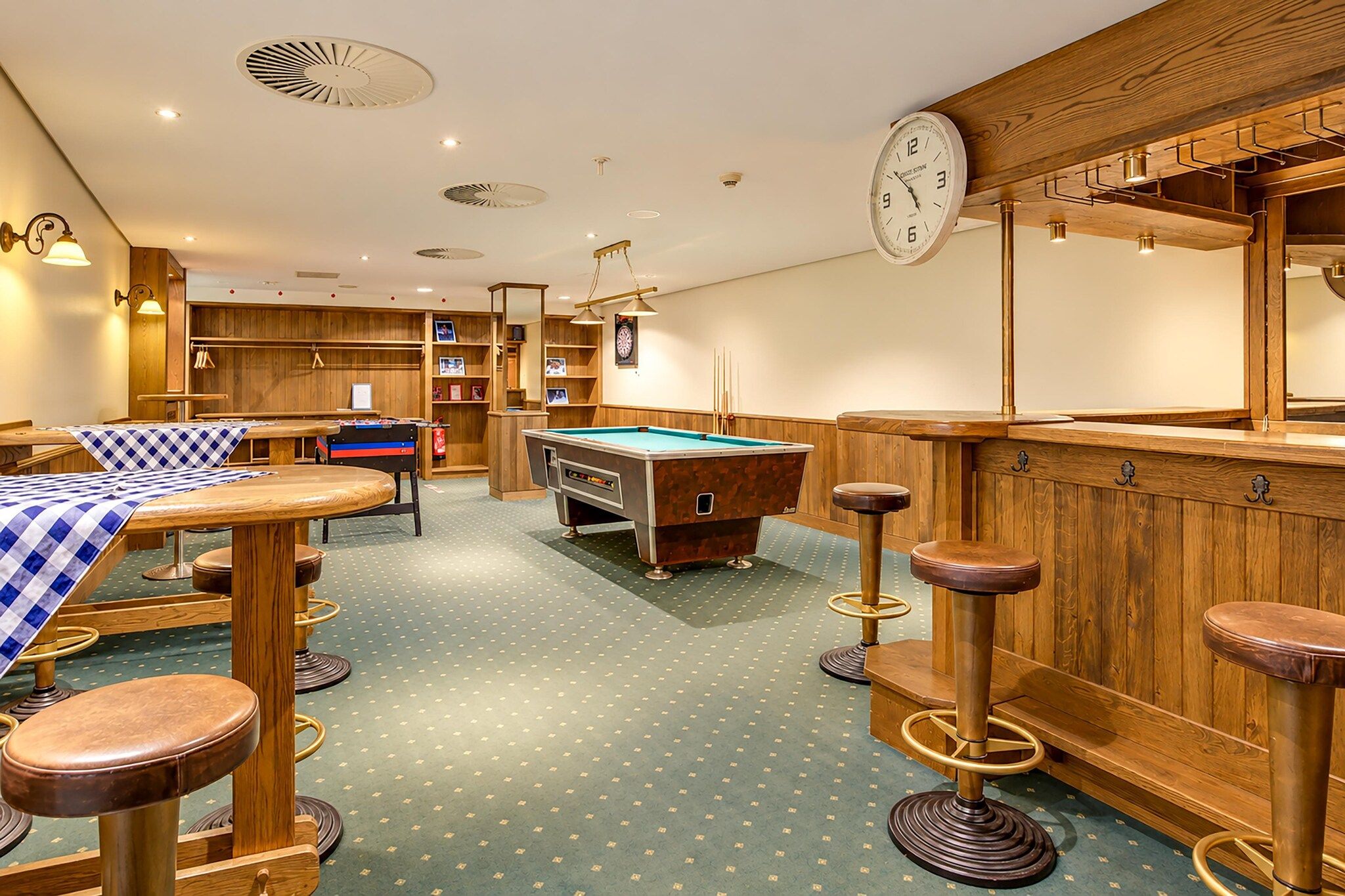 A billiards room with a pool table, stools, and a clock on the wall.