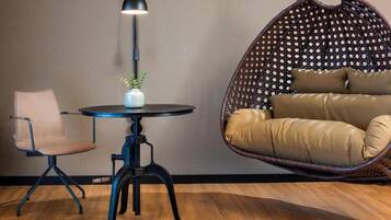 Een kamer met een ronde tafel, een stoel, een hangstoel met kussens, een hanglamp en een potplant.