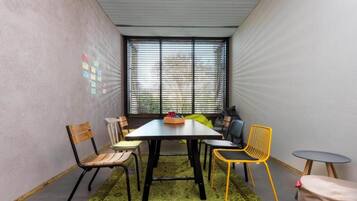 A small meeting room with a table, chairs, a rug, and a window with blinds.