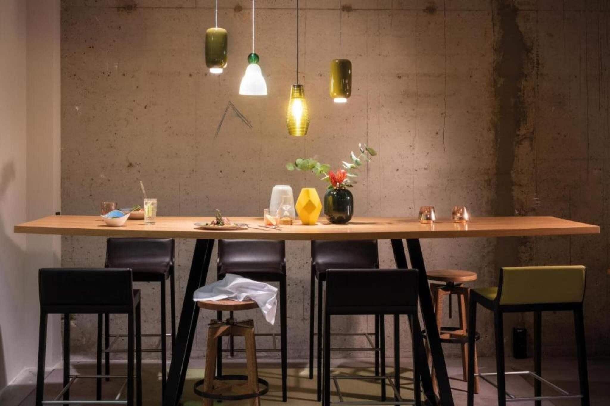 A dining area with a long table, black chairs, and hanging pendant lights.