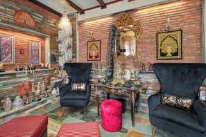 A room with a brick wall, two black armchairs, a red ottoman, a table with decorative items, and a chandelier. - Villa Eleni - Eretria's Gem with Private Pool (Eretria)