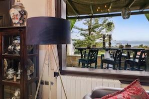 A room with a view of a tree and mountains, a table with chairs, a lamp, and a shelf with decorative items. - Villa Eleni - Eretria's Gem with Private Pool (Eretria)