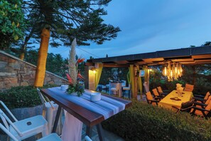 Een buitenruimte met een pergola, tafels, stoelen en een stenen muur.
