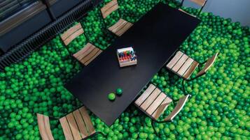 A room with a black table surrounded by wooden chairs, set in a ball pit filled with green balls.