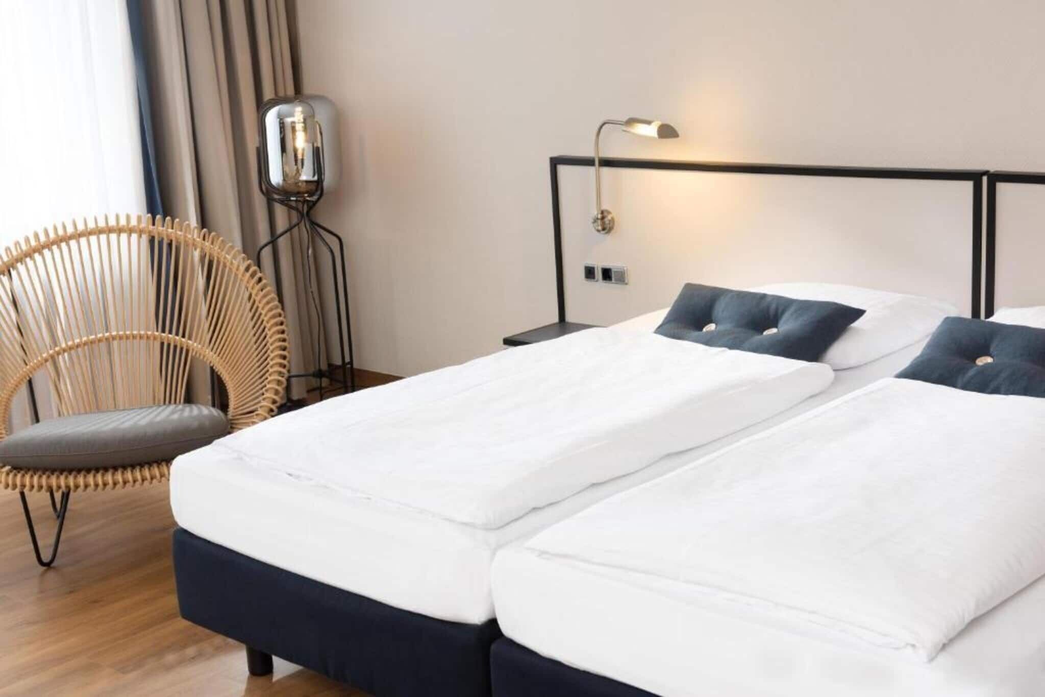 A hotel room with a double bed, a chair, a bedside table, and a wall-mounted lamp.