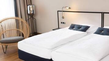 A hotel room with a double bed, a chair, a bedside table, and a wall-mounted lamp.