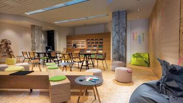A modern interior with a wooden reception desk, multiple seating areas, and a large wall with framed pictures.