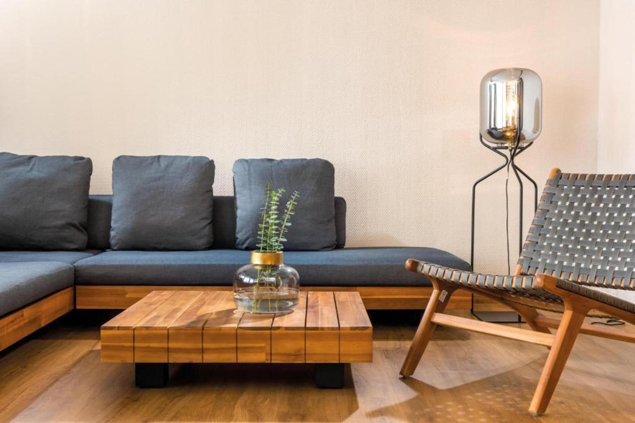 Uma sala de estar moderna com um sofá seccional, uma mesa de centro de madeira com um vaso de vidro e uma cadeira de fibra natural.