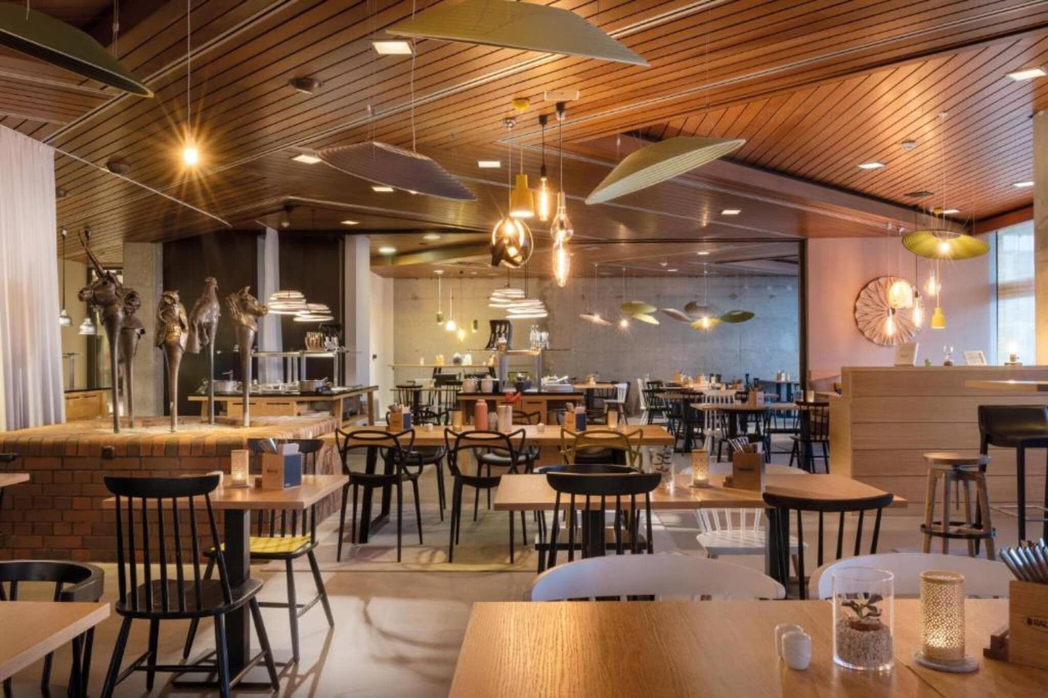 Ein modernes Restaurant mit Holzzielpaneelen, hängenden Pendelleuchten und verschiedenen Sitzgelegenheiten, darunter Tische und Stühle.