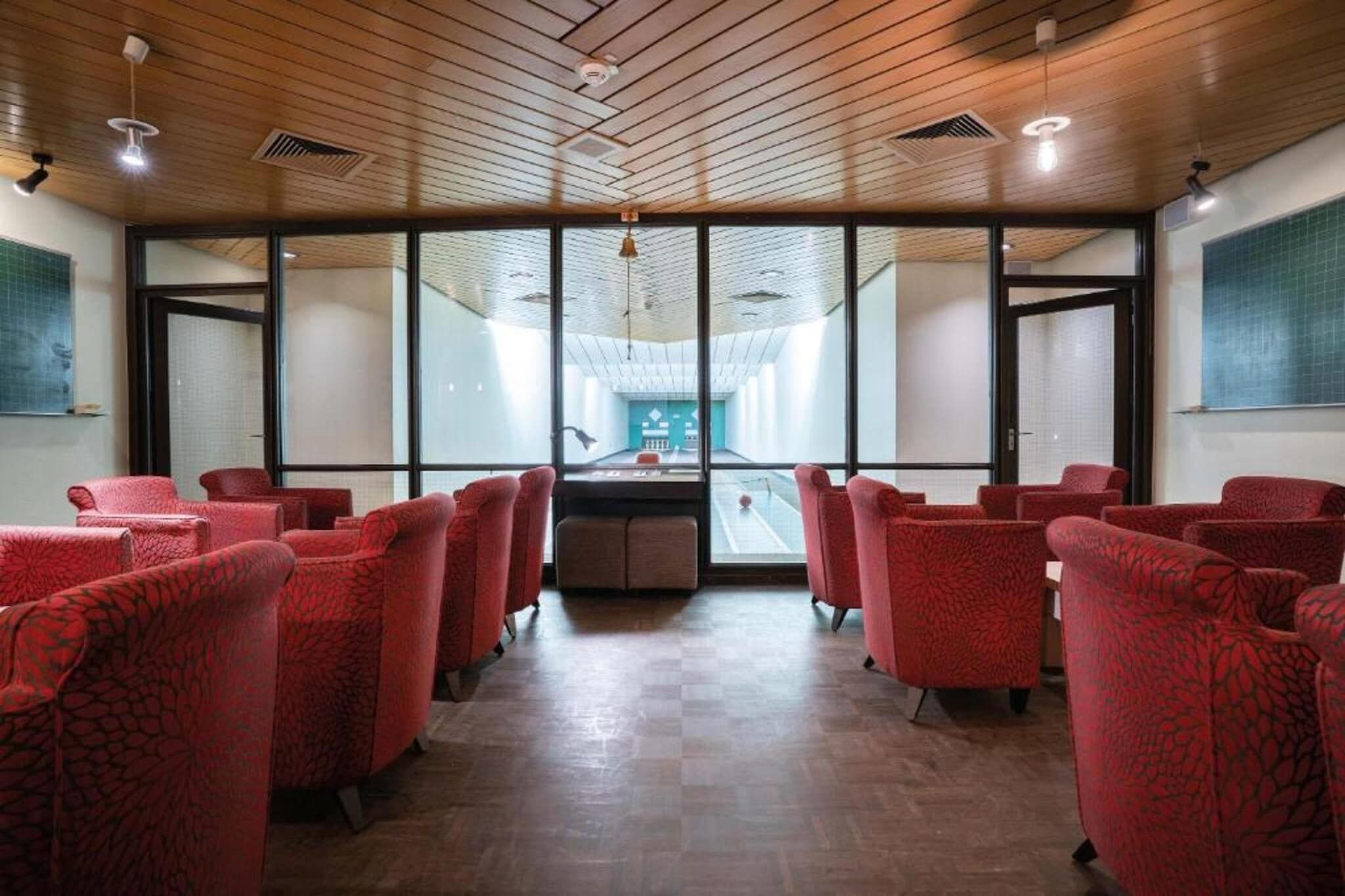Un salón de conferencias con sillas rojas, techo de madera y ventanas amplias.