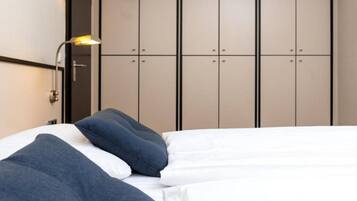 Ein Bett mit weißer und blauer Bettwäsche, eine Wandleuchte und ein Kleiderschrank mit mehreren Türen.