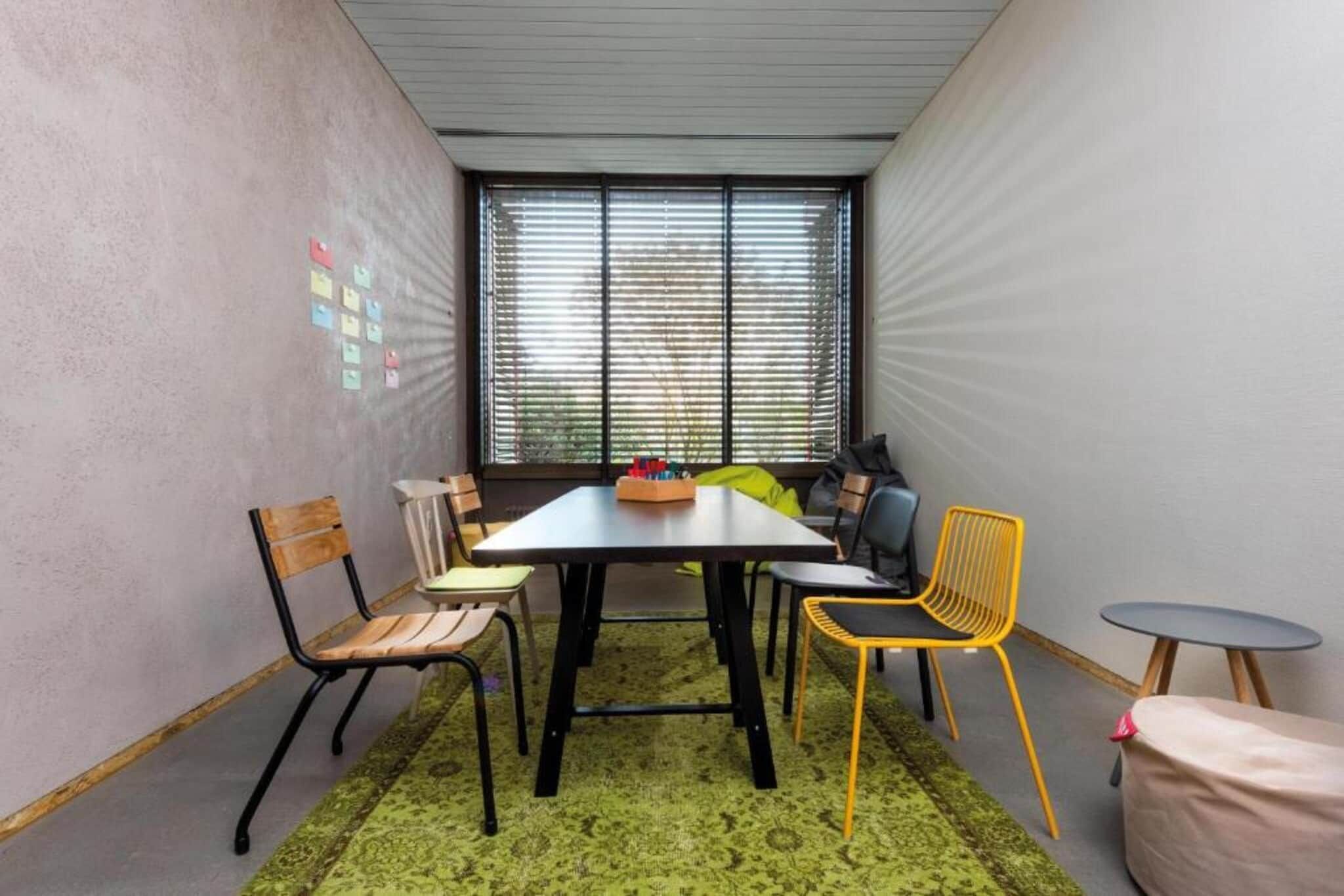 A small meeting room with a table, chairs, a rug, and a window with blinds.