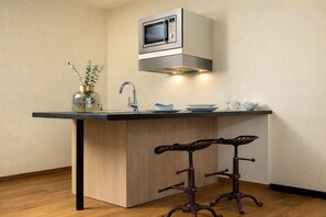 Una cocina con microondas integrado, un lavamanos y un taburete de bar.