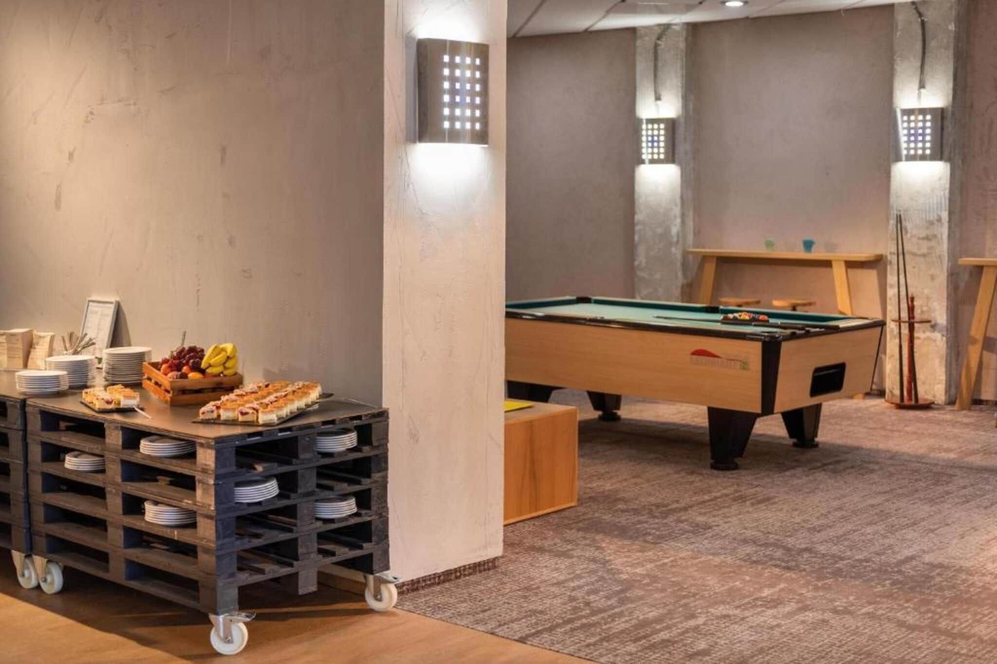 A room with a pool table, a snack bar with plates and fruit, and a billiards table.