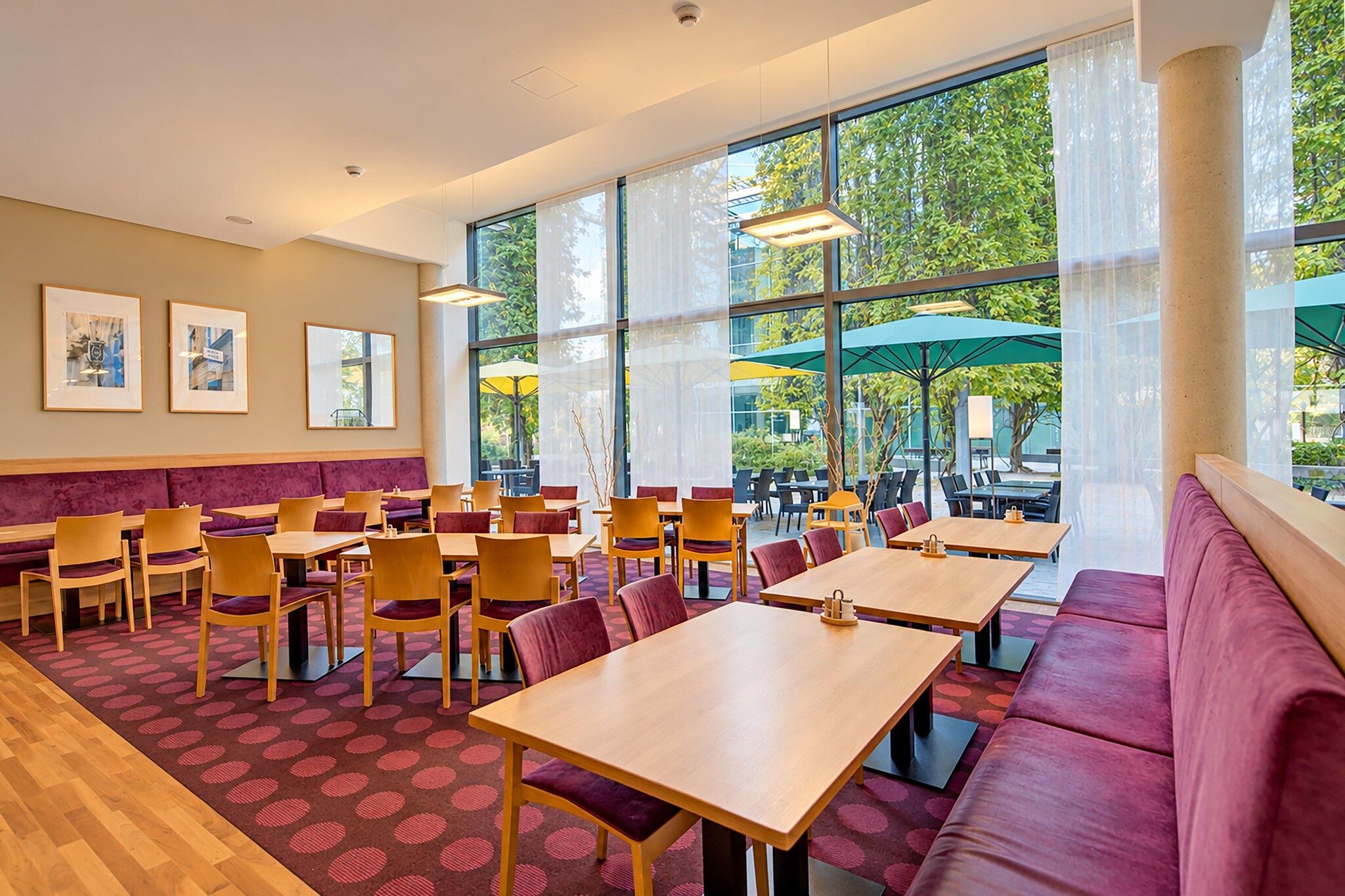 Un espace de restauration intérieur moderne, doté de tables et de chaises, de grandes fenêtres et offrant une vue sur la verdure environnante.