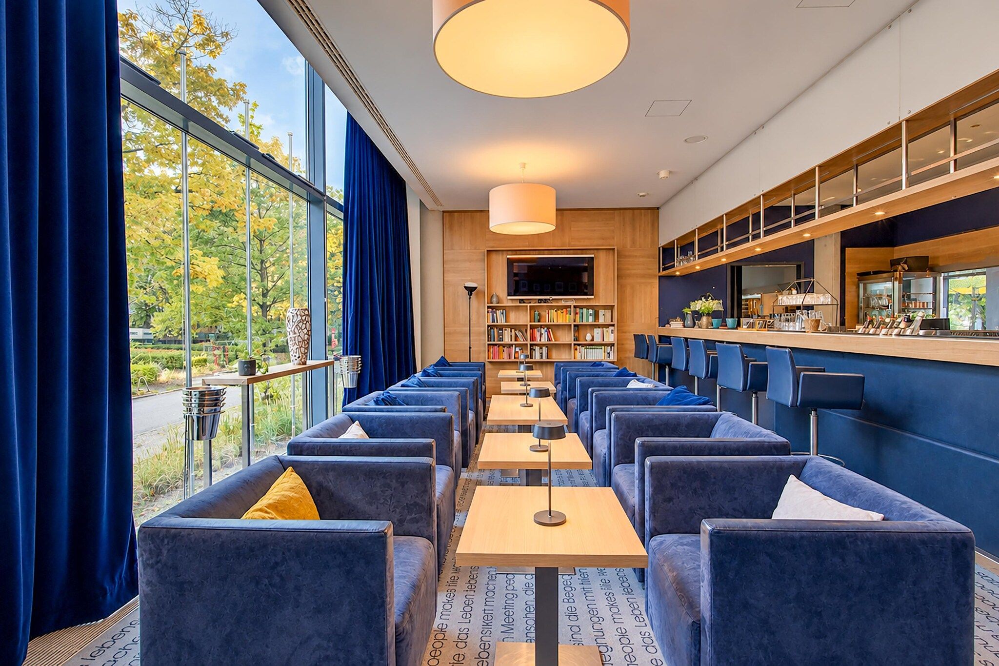 Un restaurant moderne doté d’un long comptoir, de sièges rembourrés en tissu bleu et d’une grande fenêtre donnant sur un jardin.
