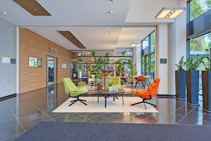 Eine moderne Lobby mit einer Sitzecke, einem Empfangsschalter und einem mit Pflanzen gefüllten Bücherregal.