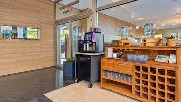 Un espace d’accueil moderne comprenant une machine à café, une vitrine et un comptoir en bois avec un porte-bouteilles à vin.