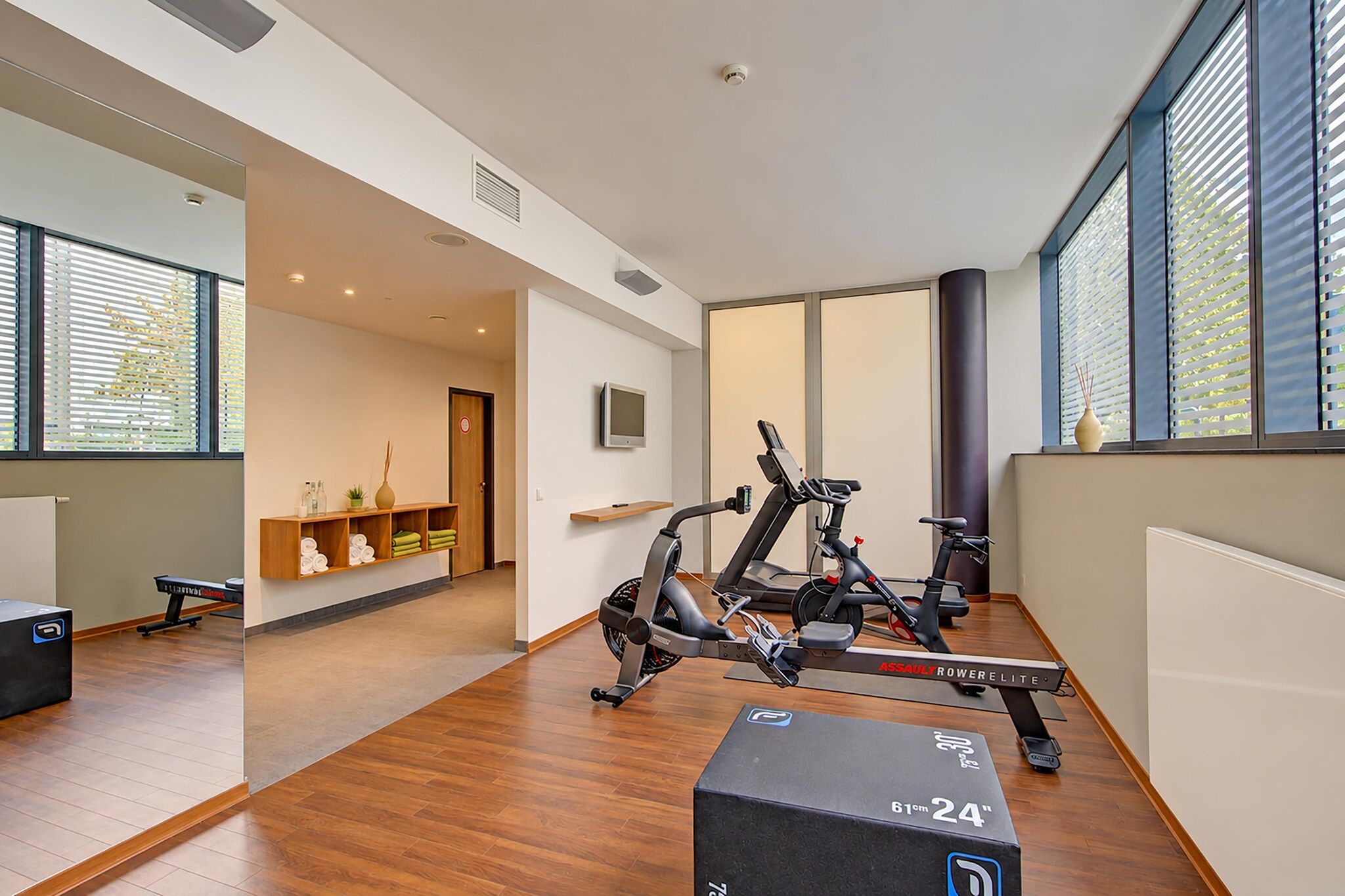 Et moderne fitnesscenter med løbebånd, en receptionsdisk og store vinduer.
