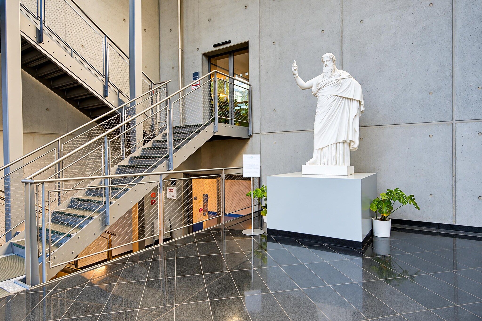 Un intérieur moderne agrémenté d’une statue en marbre, d’un escalier et de plantes en pot.