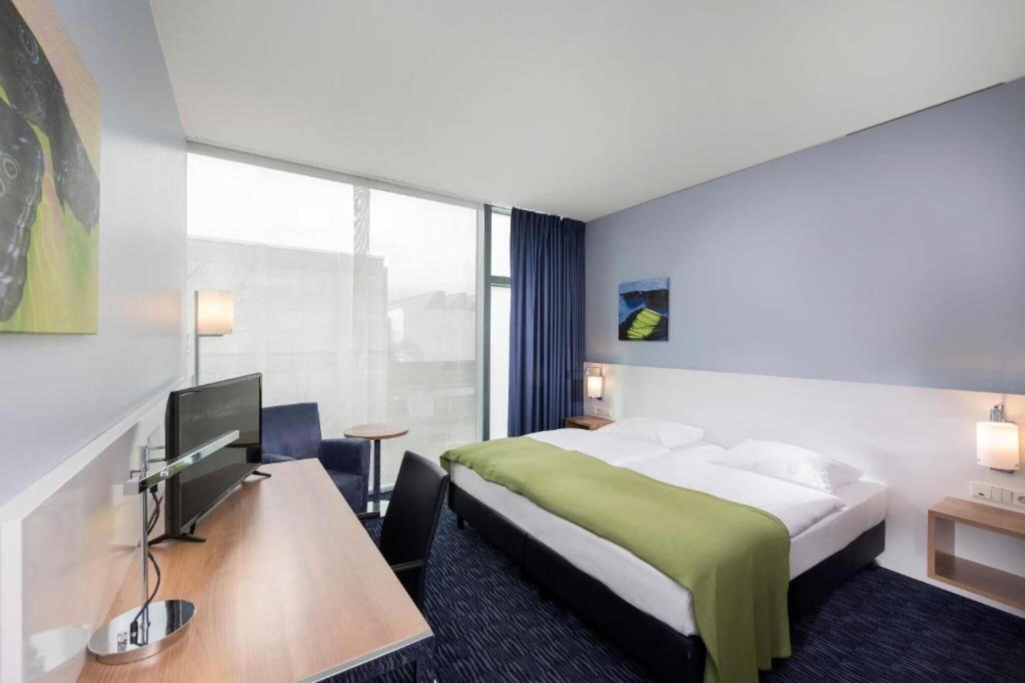 Ein Hotelzimmer mit einem Bett, einem Schreibtisch, einem Stuhl, einem kleinen Tisch und einem Fenster.