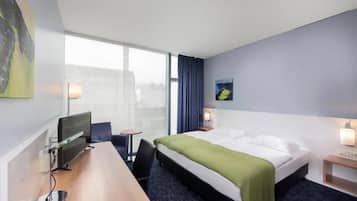 A hotel room with a bed, a desk, a chair, a small table, and a window.