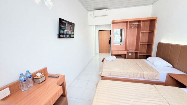 A hotel room with two beds, a wooden desk, a TV mounted on the wall, and a wardrobe.