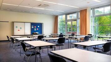 Ein Klassenzimmer mit Tischen, Stühlen, einer Tafel und einem Fenster mit Vorhängen.