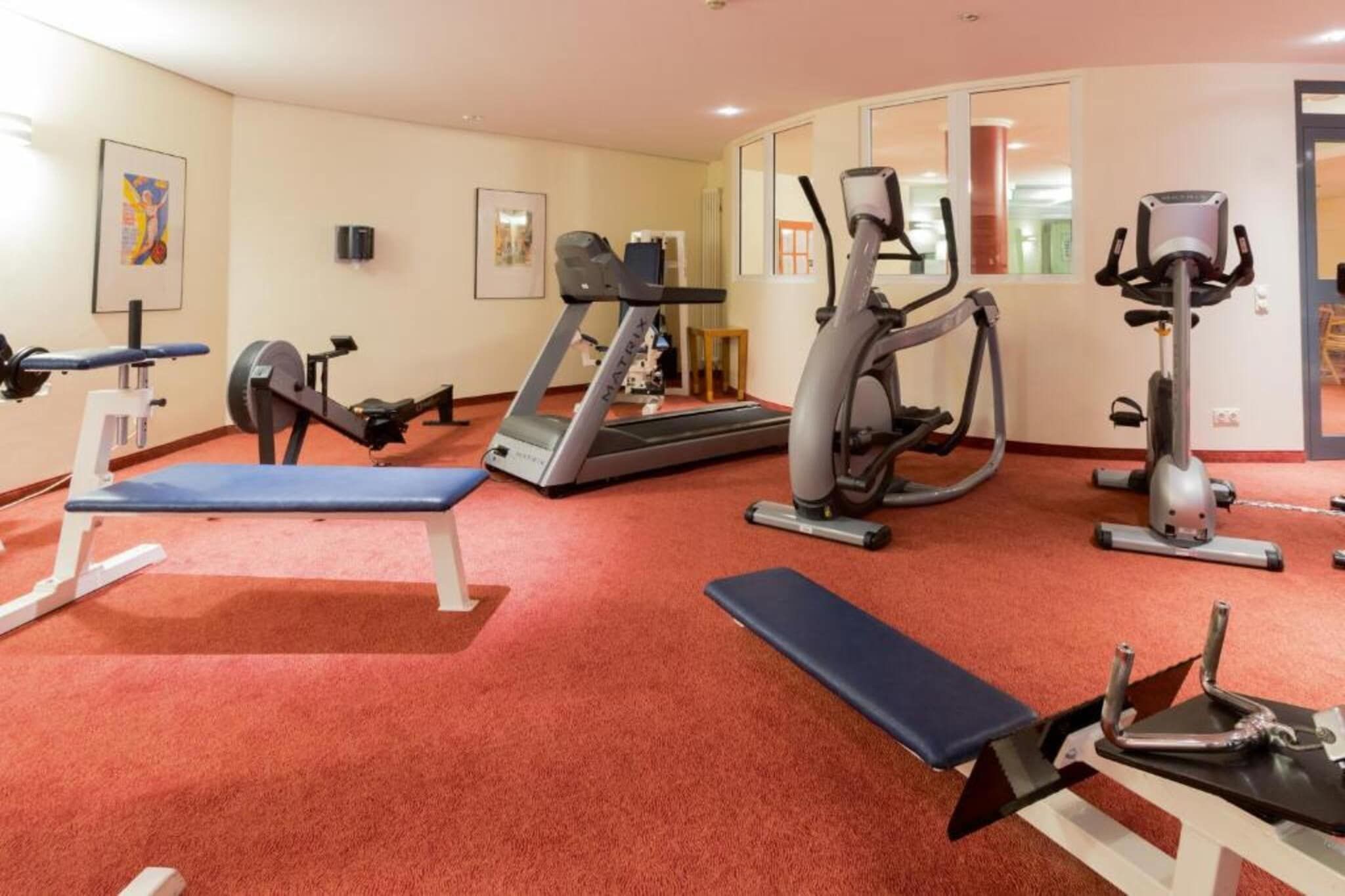 Un gimnasio con varios equipos de ejercicio, incluyendo cintas de correr, elípticas y bancos de pesas.