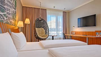 Habitación de hotel con dos camas, una silla colgante, un escritorio, televisor y ventana con cortinas.