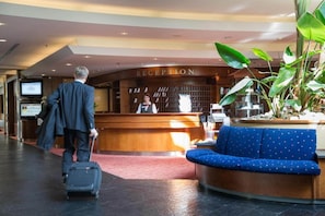 Un espace d’accueil d’hôtel avec un comptoir de réception, un canapé bleu et un homme avec une valise.