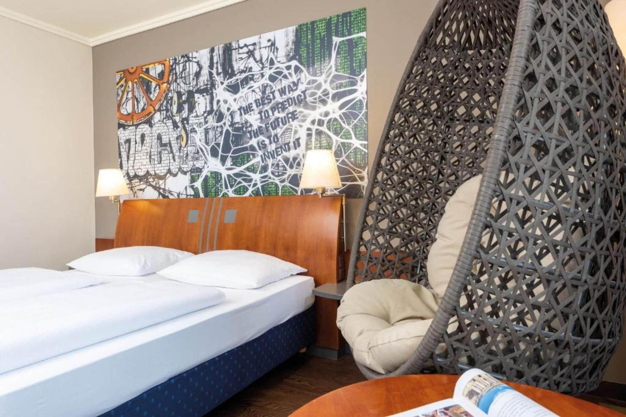 Een hotelkamer met een bed, een hangstoel en een kunstwerk aan de muur.