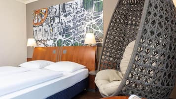 Een hotelkamer met een bed, een hangstoel en een kunstwerk aan de muur.