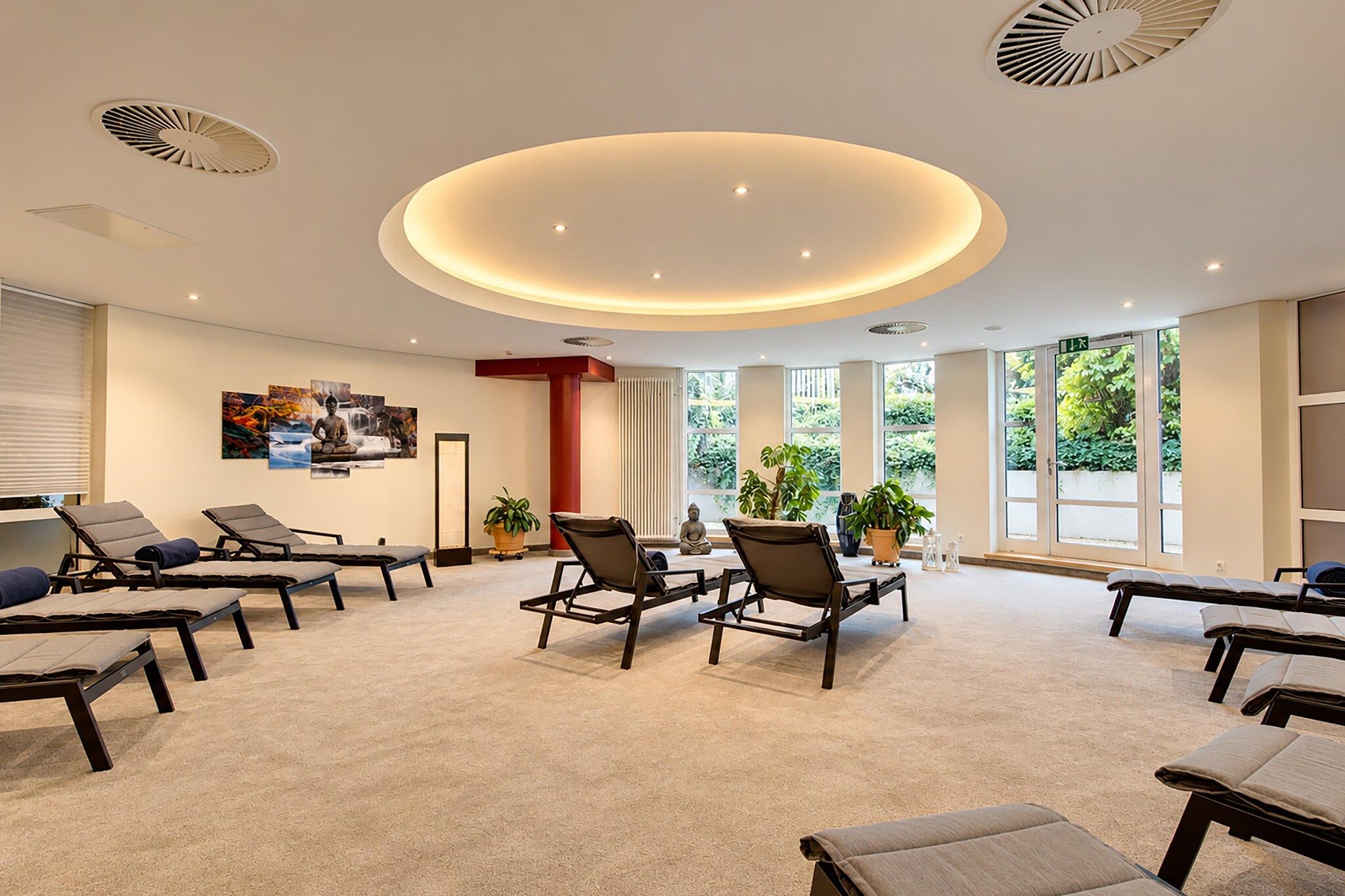 A modern spa room with multiple massage tables, a central seating area, and large windows providing natural light.