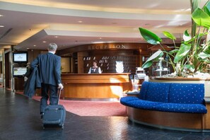 Zona de recepción de hotel con un mostrador, un sofá azul y un hombre con una maleta.