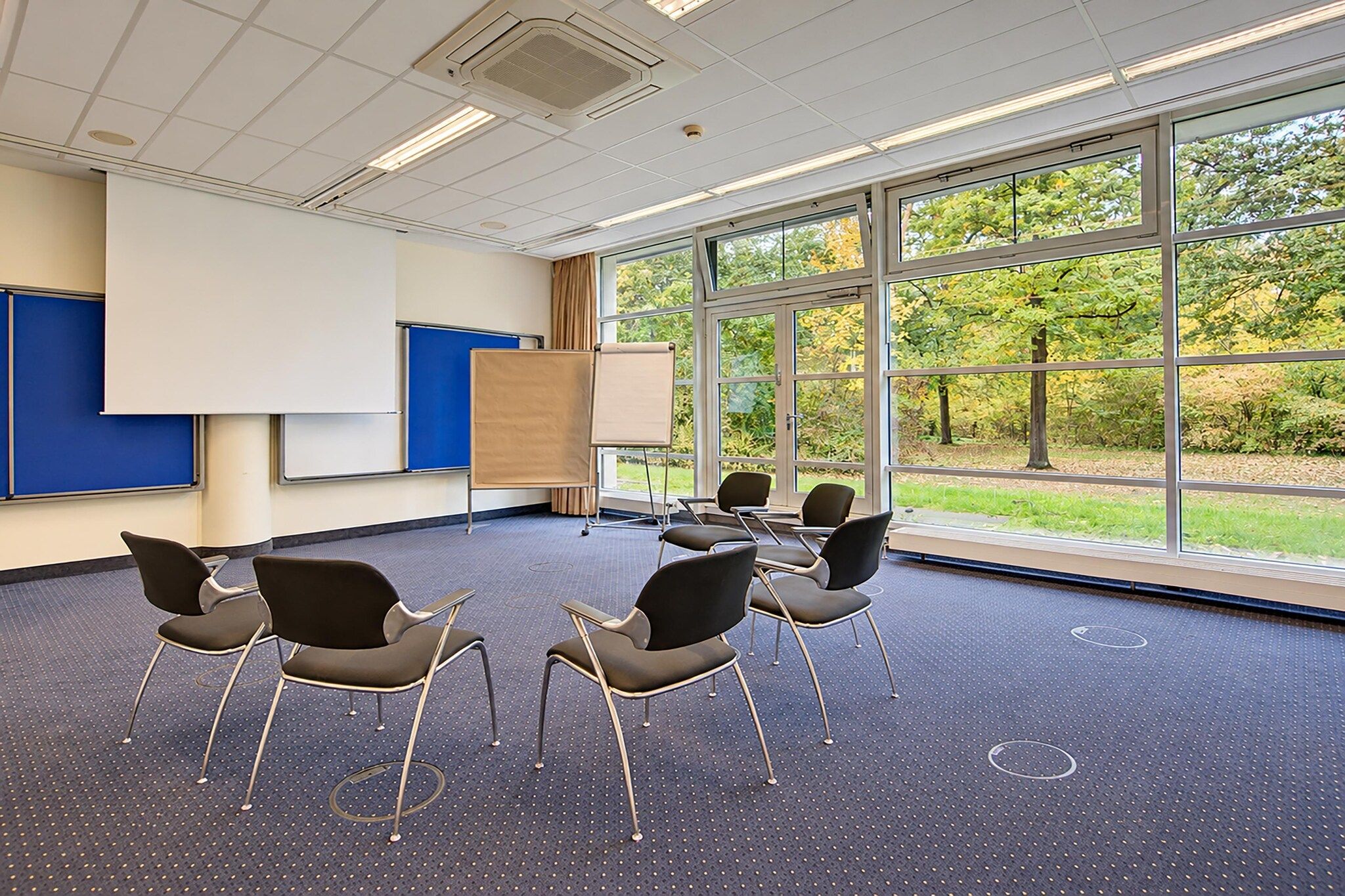 Ein Konferenzraum mit großem Fenster, einer Whiteboard und mehreren Stühlen, die um einen Tisch angeordnet sind.