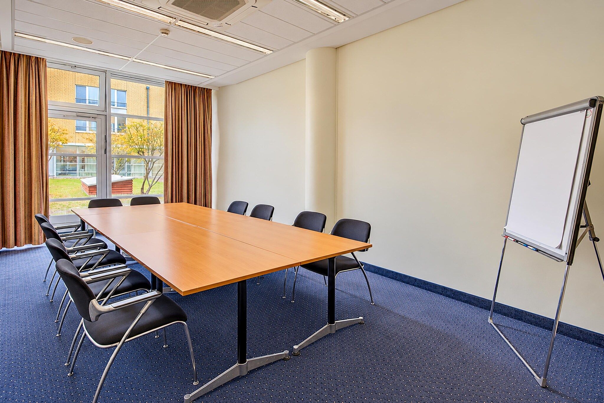 Ein Konferenzraum mit einem großen Tisch, Stühlen, einer Whiteboard-Tafel und Blick ins Freie durch große Fenster.