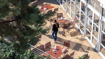 Un patio exterior con mesas y sillas, una persona caminando y un edificio con ventanas de vidrio.