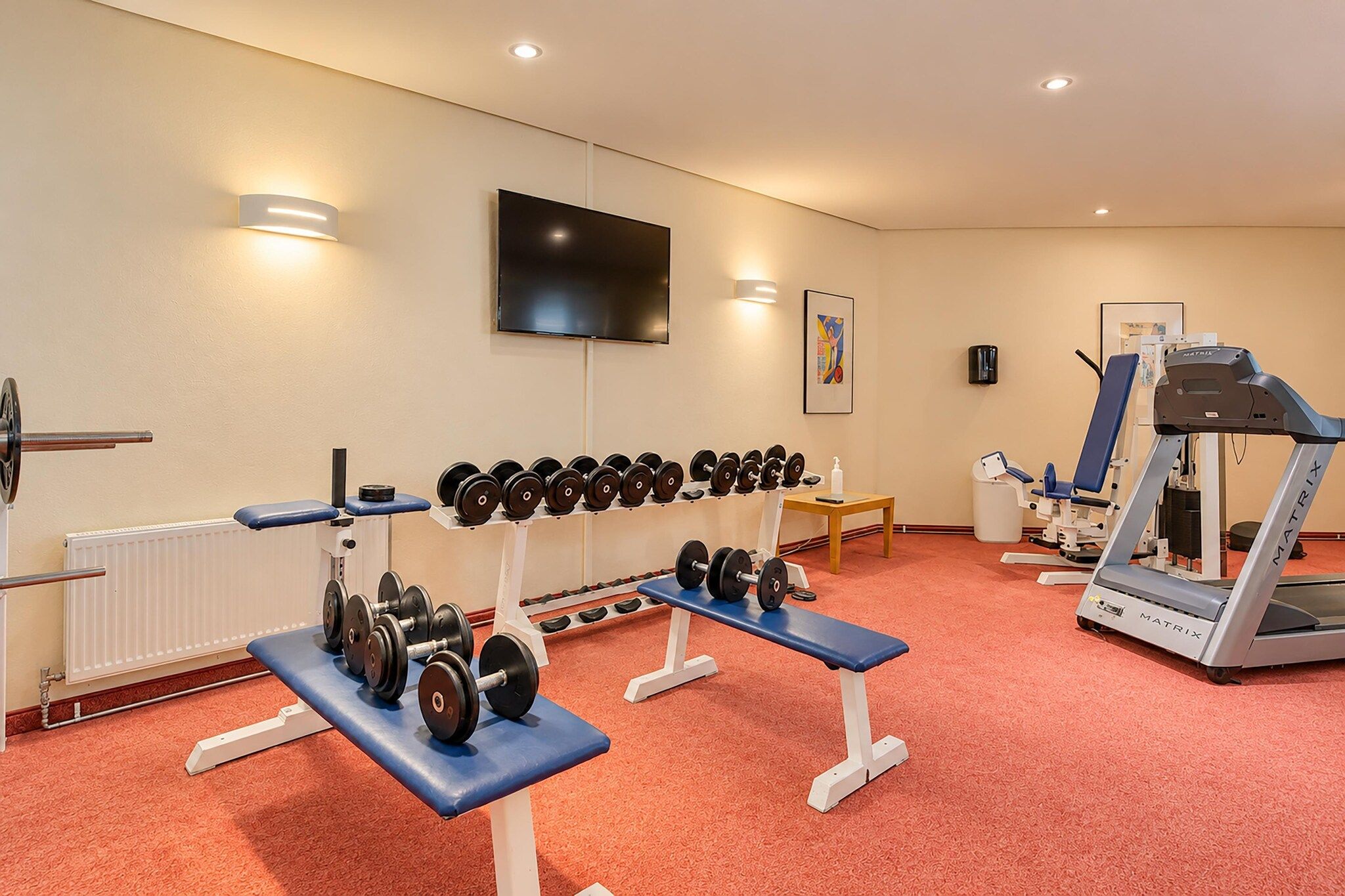 Ein Fitnessraum mit Trainingsgeräten, einem Fernseher und einer Heizung.