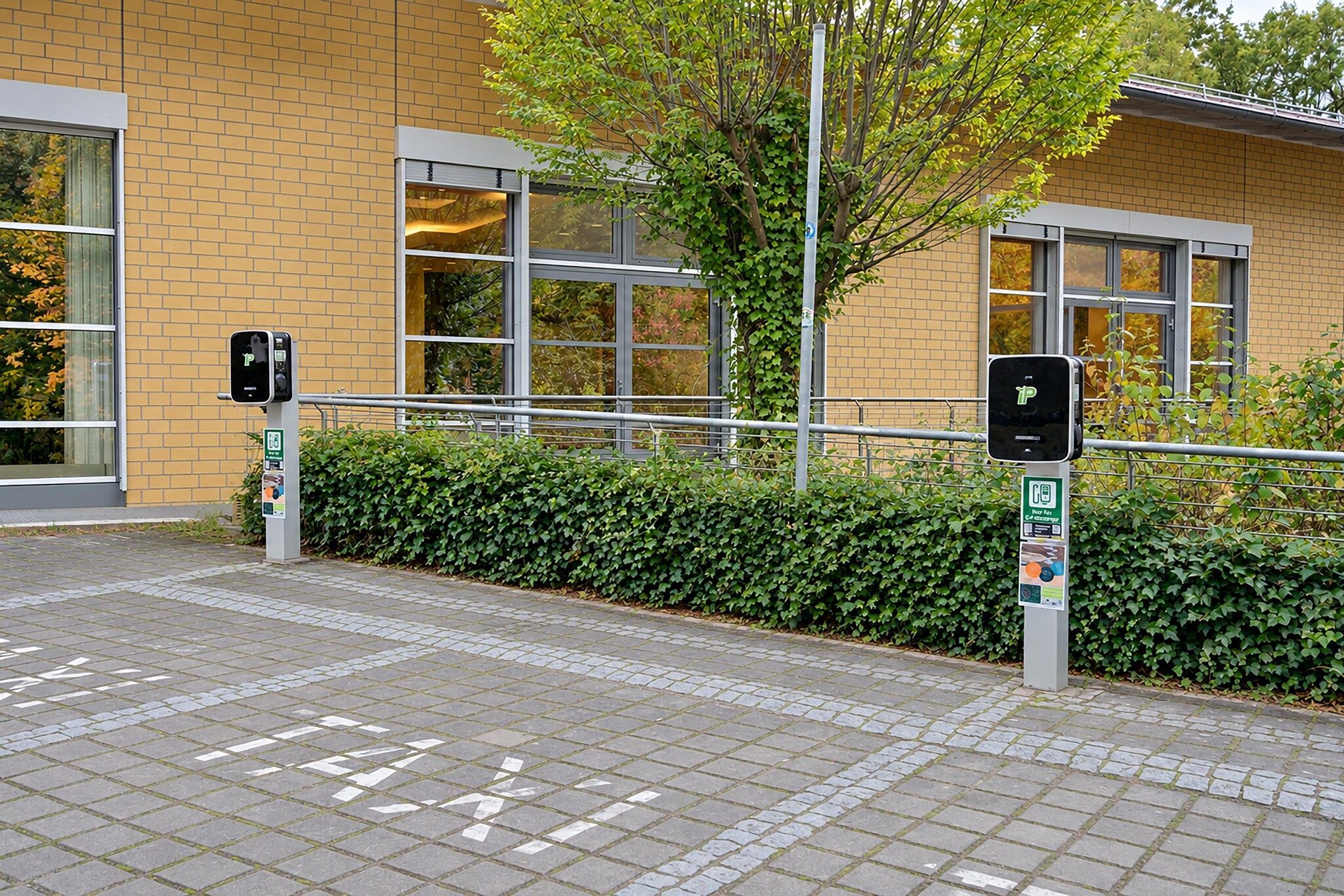Ein Parkplatz mit Ladestationen für Elektrofahrzeuge und ein Gebäude mit großen Fenstern und einer Ziegel-Fassade.