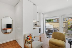 A modern living room with a sofa, a chair, a TV, and a kitchen area with a stove. - Porto Garden Patio Retreat (Porto)