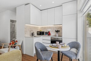 A compact kitchen with white cabinets, a built-in stove, and a dining area with two chairs. - Porto Garden Patio Retreat (Porto)