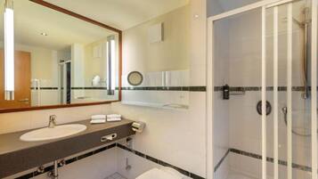 Baño de hotel con lavamanos, espejo, toallero y cabina de ducha con mampara de vidrio.