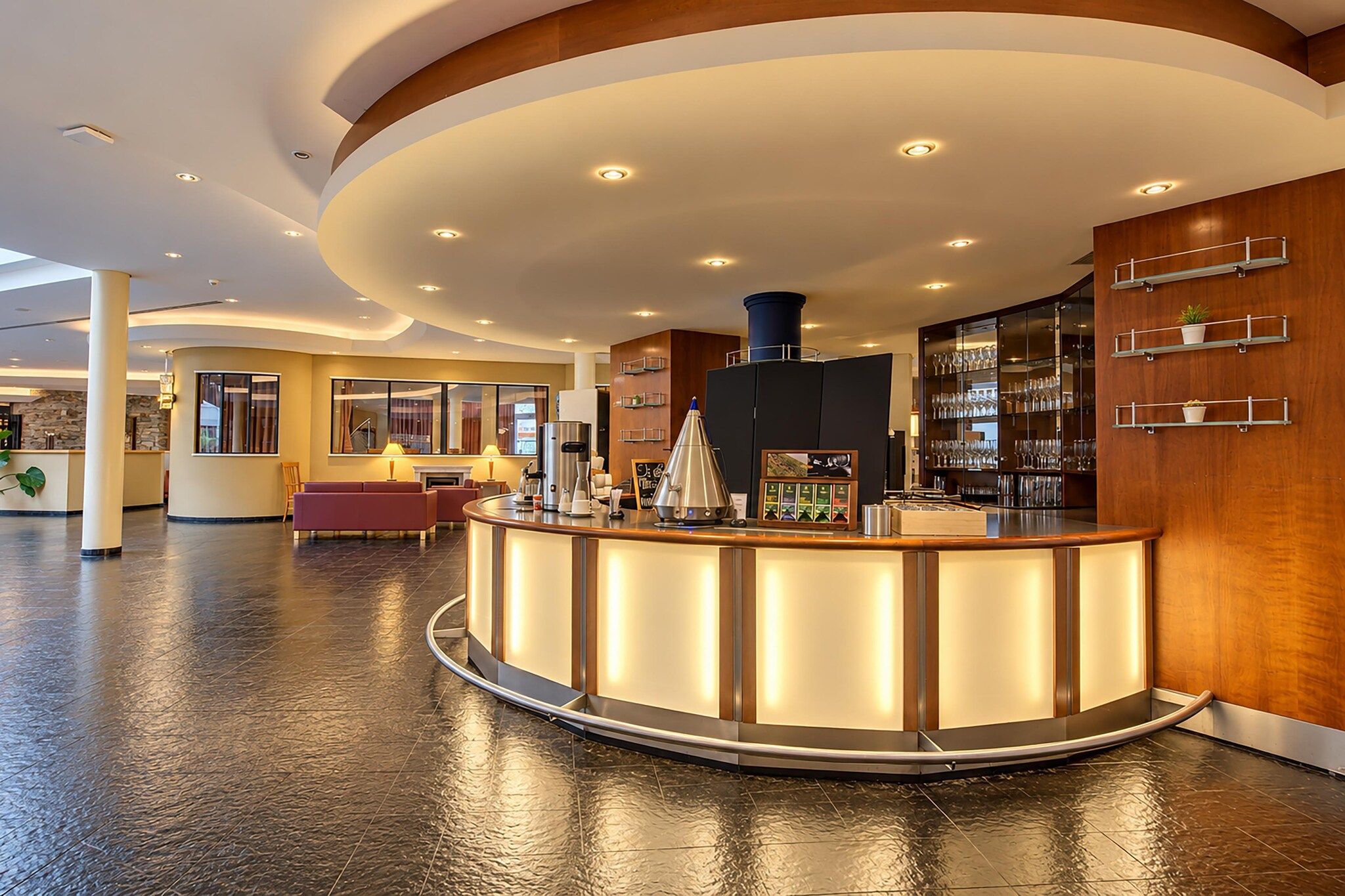 Eine Hotelhalle mit einer zentralen Rezeption, einer Sitzecke und einer Bar mit Regalen.